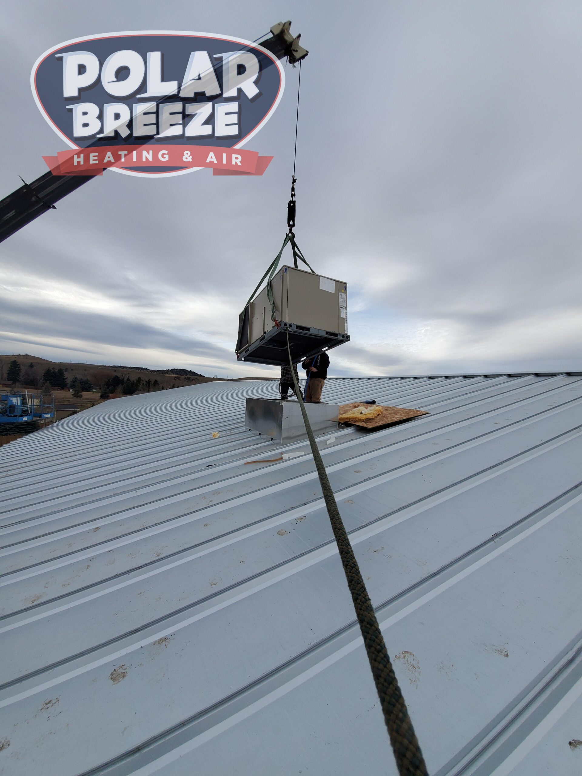 A crane lifts an HVAC unit onto a metal rooftop under cloudy skies; Polar Breeze Heating & Air logo is in the upper left corner.