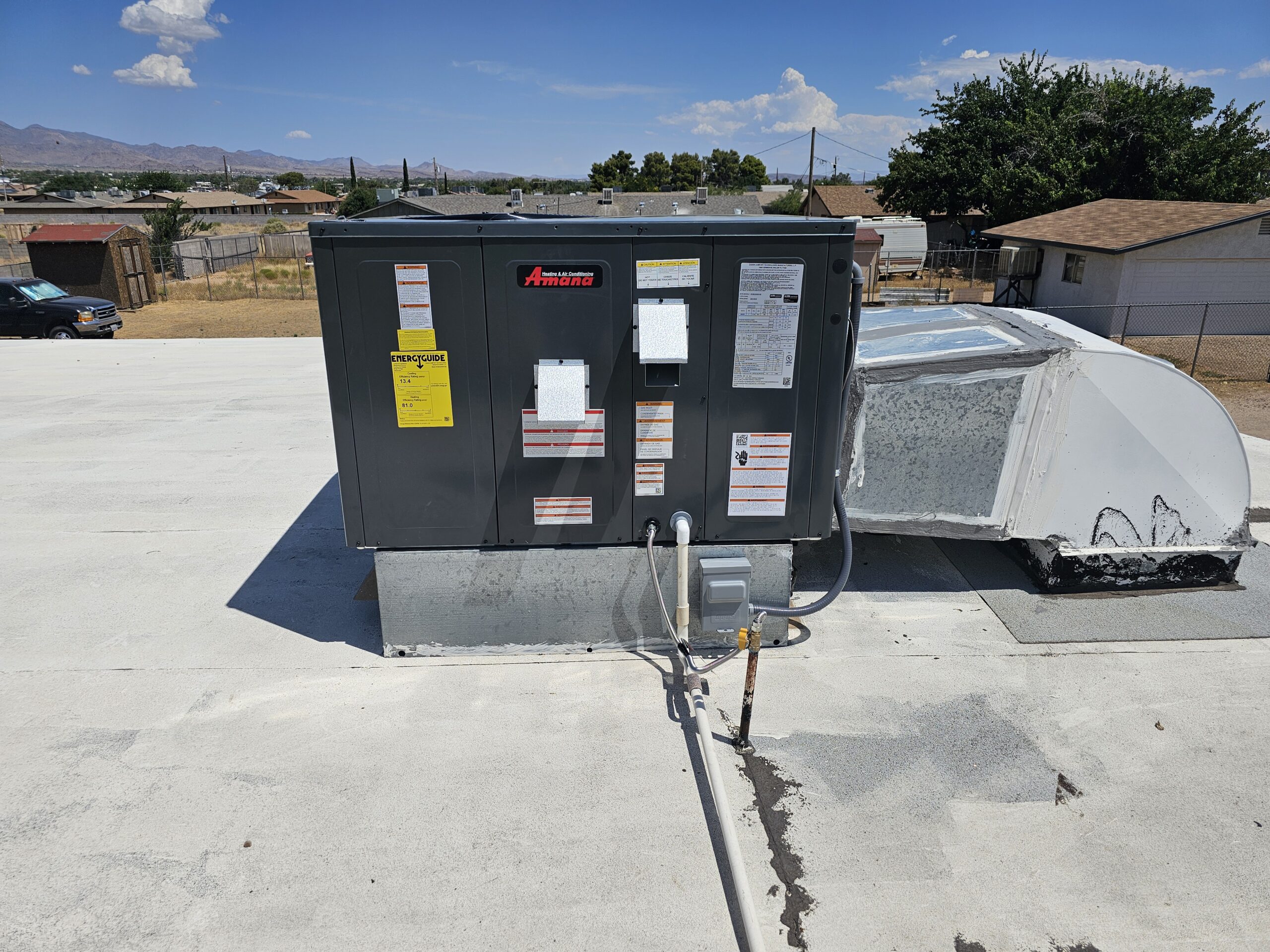 Large HVAC unit installed on a flat rooftop with visible ductwork, electrical connections, and warning labels under a clear blue sky.